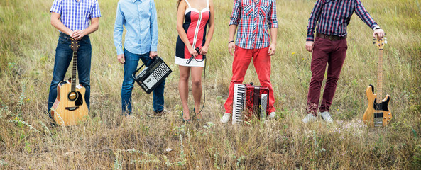 Concept photo of music band with guitars, microphone and accordion standing outdoors