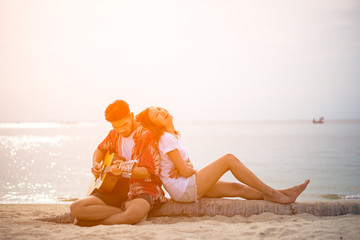 Cute hispanic couple playing guitar serenading on beach in love and embrace