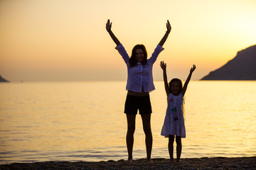 Fototapeta premium Mother and daughter lifting arms while standing on the beach at sunset