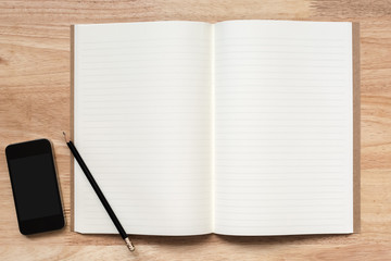 Top view of open notebook with two blank pages, pencil and smart phone on wooden table