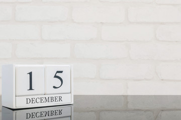 Fototapeta na wymiar Closeup white wooden calendar with black 15 december word on black glass table and white brick wall textured background with copy space , selective focus at the calendar