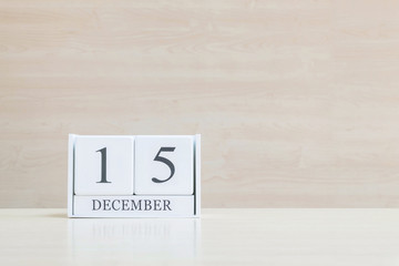 Closeup surface white wooden calendar with black 15 december word on blurred brown wood desk and wood wall textured background with copy space , selective focus at the calendar
