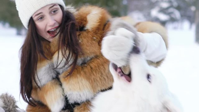 The girl playing with husky dog in snow which biting her hand. Slow motion