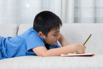 Bored Asian Chinese little boy writing book on the sofa