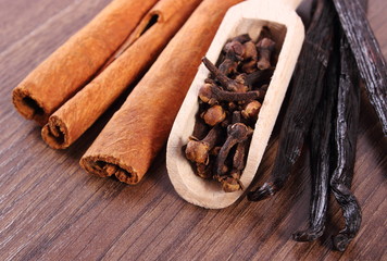 Closeup of cloves, fragrant vanilla and cinnamon on wooden surface plank