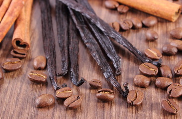 Fragrant vanilla, cinnamon sticks and coffee grains on wooden surface