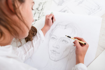 Fototapeta premium Artist drawing pencil portrait close-up. Woman painter creating picture of woman on big whatman. Art, talent, craft, hobby, occupation concept