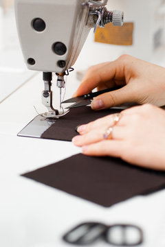 Hands cutting thread on sewing machine side view. Seamstress stitching dark fabric on work equipment. Garment industry, tailor workshop, designer workshop concept