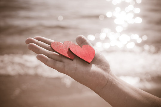 two red hearts on the palm of the girl on sea wave background 