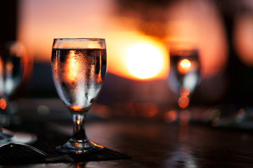 glass of water on the table with beautiful, colorful sunset at background