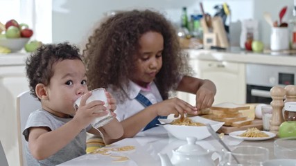 Little brother and sister eating dinner together: boy dropping milk and spaghetti on table and mom taking care of him
