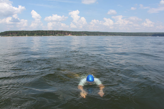 The young man swimming in the river in a blue cap