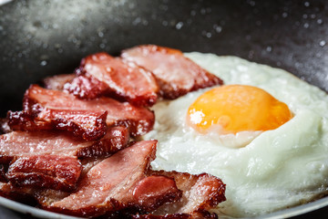 Slices of smoked bacon and fried egg in frying pan