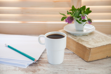 Office workplace with  coffee cup on wooden desk table in front of window with blinds, selective focus
