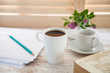 Office workplace with  coffee cup on wooden desk table in front of window with blinds, selective focus