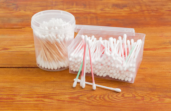 Two different cotton swabs in plastic containers on old planks