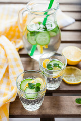 the refreshing drink with a lemon, a cucumber and rosemary in a glass on a table, selective focus