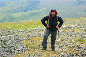 Happy smiling man standing with backpack in the mountains hiking