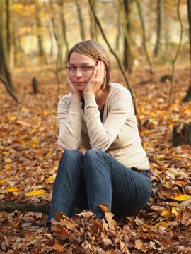 Sad young woman sitting in the autumn forest