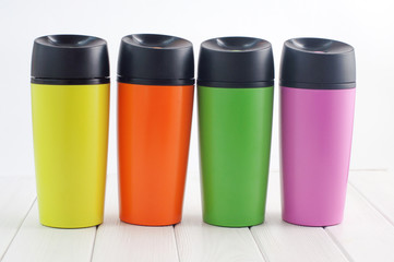 Color thermos mugs on the white wooden table