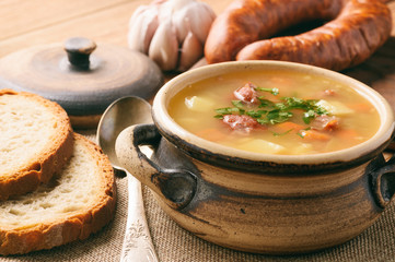 Pea soup with smoked sausage on brown wooden background.