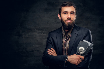 A bearded man dressed in a suit holds vintage 8mm video camera.
