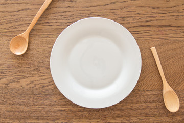 spoons with empty white plate on wood table