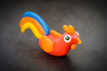 Plasticine rooster cock on a dark background.