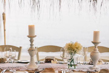 Burning white candles stand on dinner table on the beach