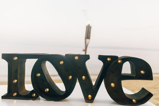 Black steel lettering LOVE stands on white table on the beach