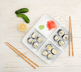 Square plate with rolls on a wooden table, ginger, cucumbers, lemon. View from above
