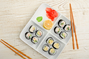 Square plate with rolls on a wooden table, ginger, lemon and wasabi. Top view