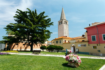 Fototapeta na wymiar Euphrasian basilica bell tower and a park with green grass in the summer in Porec, Croatia.