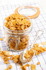cornflakes in a glass storage container with spoon on a kitchen