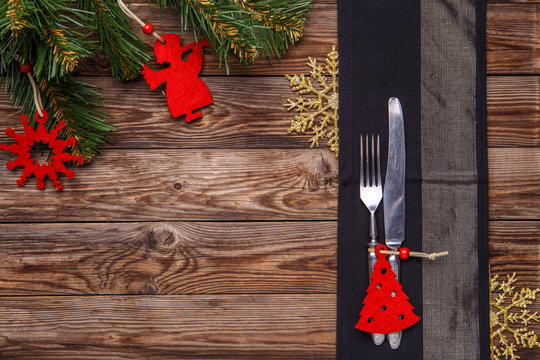 Christmas table place setting with fork and knife, decorated christmas toy, gold snowflakes and christmas pine branches.
