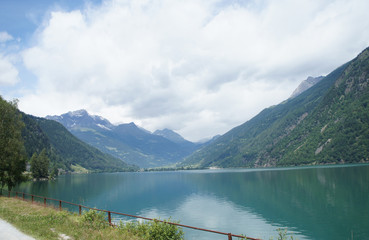 Fototapeta na wymiar Lago di Poschiavo in Graubünden/Der Lago di Poschiavo ist ein natürlicher See im Süden von Graubünden in der Schweiz; er ist umrahmt von Bergen; leichte Spiegelung; blauer Himmel und Wolken