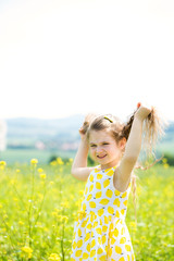 Charming happy little girl playing with her hair in a canola fie