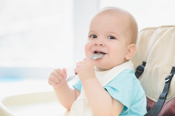 baby holding a spoon in his mouth and laughs