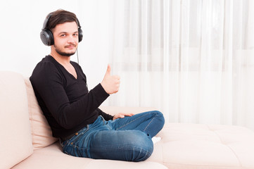 Obraz premium Man sitting on sofa wearing headphones showing thumb up