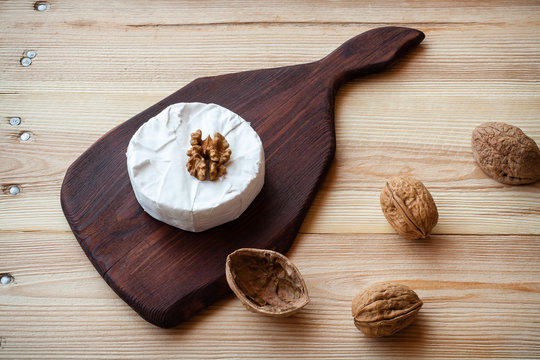 Sliced round camembert cheese on a wooden board with nuts. Rustic style and natural light. Top view. Vintage burlap napkin background.
