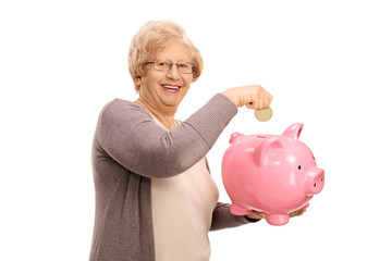 Happy elderly woman putting a coin into a piggybank