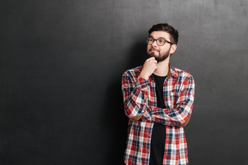 Smiling thoughtful young man un glasses standing and thinking