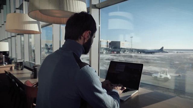  A student    working  on laptop  sitting to terrace near the window in cafe  at the airport 