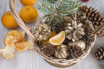 Christmas holidays composition: wicker basket with cones, mandarins,golden nuts on light wooden background top view
