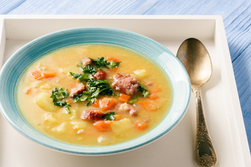 Pea soup with smoked sausage on blue wooden background.