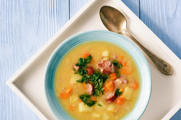 Pea soup with smoked sausage on blue wooden background.