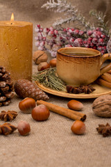 Cup of coffee, walnuts, hazelnuts, cinnamon sticks, star anise, cone, candle, fir branch on sackcloth fabric