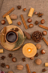 Obraz na płótnie Canvas Cup of coffee, cookies, walnuts, hazelnuts, cinnamon sticks, star anise, cone, candle, fir branch on sackcloth fabric