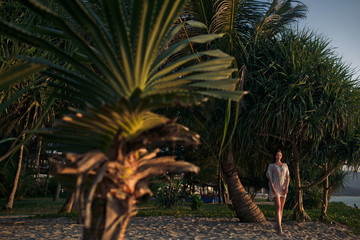 Fototapeta premium young and beautiful woman walks along the beach near palm trees