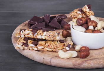 Granola bars, nuts, and  chocolate on wooden cutting board. - 129571578